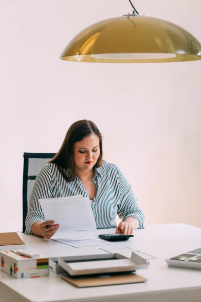 istock Smiling Overweight Businesswoman Analyzing Financial Reports Using a Calculator 1588097756