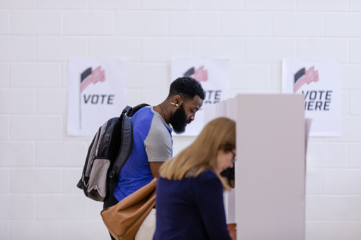 Diverse people stand in a row at the voting booths to vote during the election.