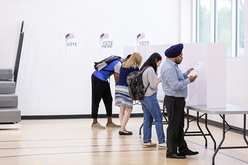 A multiracial group of citizens use paper ballots in private voting booths to vote in the election.