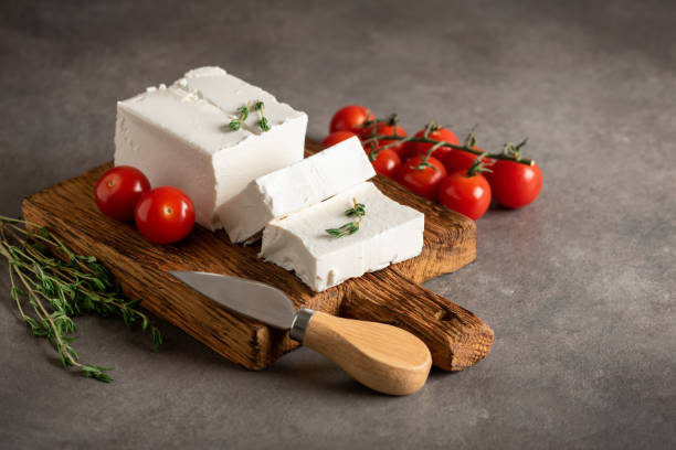 istock Feta cheese on a wooden board with thyme and cherry tomatoes. Brown rustic background. Side view, selective focus. 1588106658