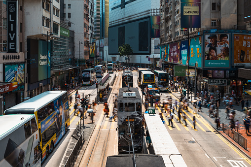 Motion blur of Chinese people walk cross zebra crossing at Causeway Bay, Hong Kong shopping district. Tram, bus, car and taxi traffic transportation. Asia transport city life, Asian tourism concept