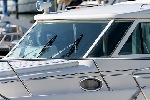 Cab of white luxury leisure motor boat with wipers headlights and windshield as partial view window porthole