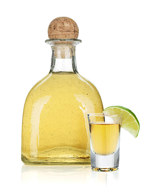 Bottle of gold tequila next to lime garnished glass Bottle of gold tequila. Isolated on white background tequila slammer stock pictures, royalty-free photos & images