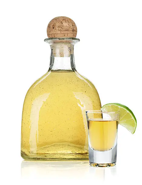 Photo of Bottle of gold tequila next to lime garnished glass