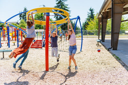 A group of tween girls and boys have fun playing together on a jungle gym play structure during school recess on a sunny afternoon.