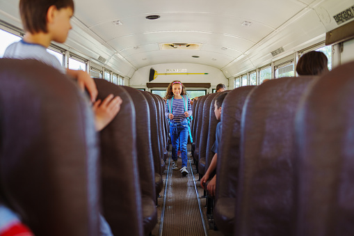 A cute elementary age girl walks down the aisle of a school bus to get off at her bus stop.