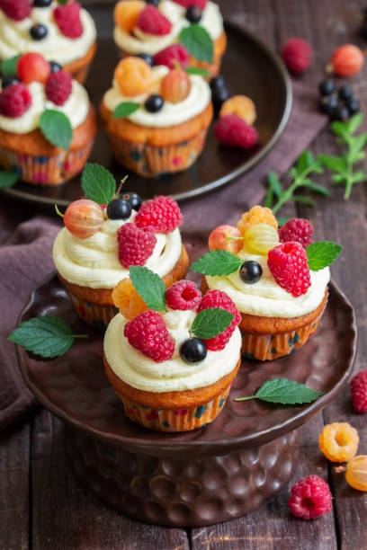 istock Cupcakes with butter cream and raspberry curd, decorated with berries on a wooden surface. 1588259228