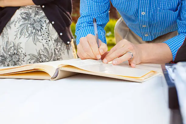 A man and a woman sign a wedding guestbook with a pen.