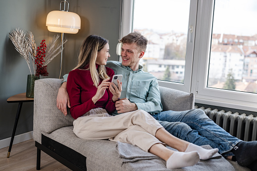 Young man and woman sitting relaxed on the sofa and using phone