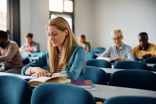 Mid adult female student reading book while attending a class at the university.