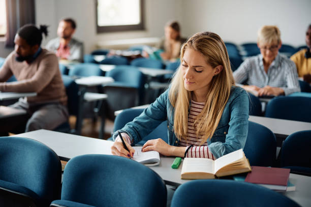 istock Mid adult woman writing in notebook while attending a class at the university 1588286833