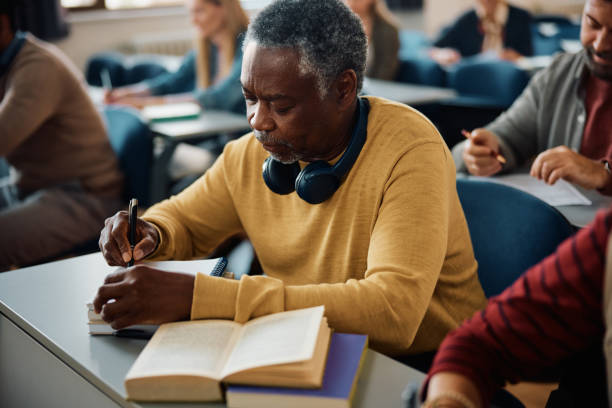 istock Senior black man writing notes while learning during adult education training class in the classroom. 1588288392