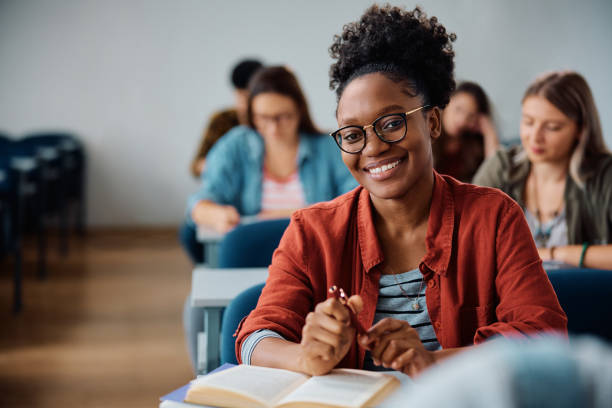 Happy black females student during a class in lecture hall looking at camera. Happy African American woman attending a lecture in university classroom and looking at camera. adult student stock pictures, royalty-free photos & images