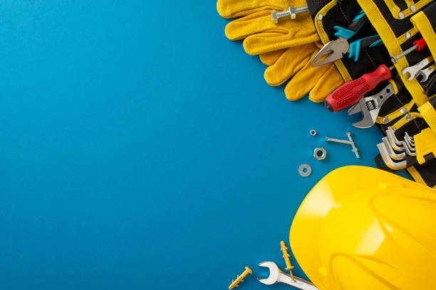 Honoring contributions of construction workers on Labor Day: this top-view photo featuring flag, construction helmet, work gloves and building tool on blue backdrop. Ideal for advertisements or text