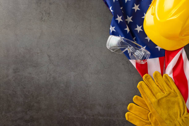 istock Celebrating the tireless efforts of construction workers on Labor Day. Top-down image showcasing flag, helmet, gloves and goggles on grunge textured grey concrete. Copyspace available for ads or text 1588323083
