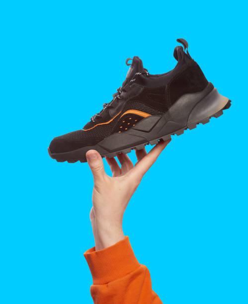 istock Stylish black sneaker with chunky sole in man's hand, isolated on a bright blue background. Mock-up for advertising a sports footwear shop 1588336002