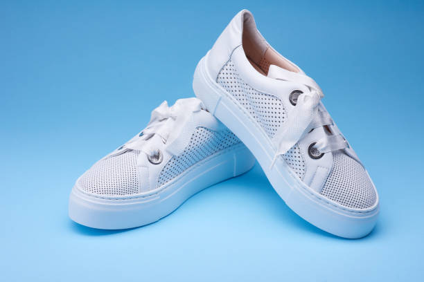 istock Comfortable women's white sneakers from perforated leather with white rubber sole on the gradient blue background. Concept of the sport casual footwear 1588336529