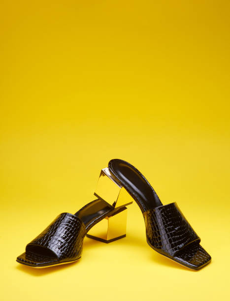 istock Bold black reptile leather flip-flops with metallic block heels, isolated on a bright yellow background. Copy space for text. Fashionable stylish party shoes 1588337604