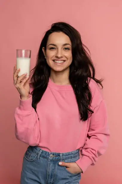 Photo of Attractive young female with a happy smile showing her favorite dairy drink during the studio photo shoot. Healthy beverage concept