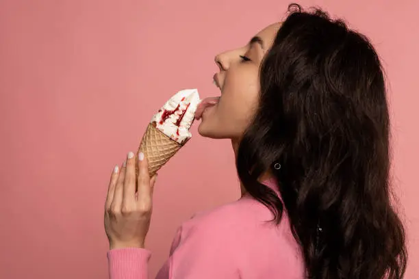 Photo of Beautiful brunette eating an appetizing sundae with her eyes closed in front of the camera. Favorite sweet food consumption concept