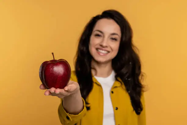 Photo of Female with a radiant smile showing her favorite fruit in front of the camera against the yellow background. Healthy food concept