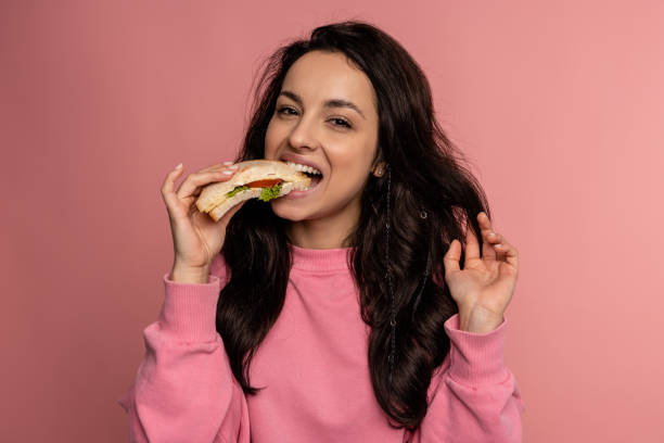 istock Hungry young dark-haired lady dressed in the jumper enjoying her nutritious sarnie in front of the camera. Healthy snack concept 1588352680