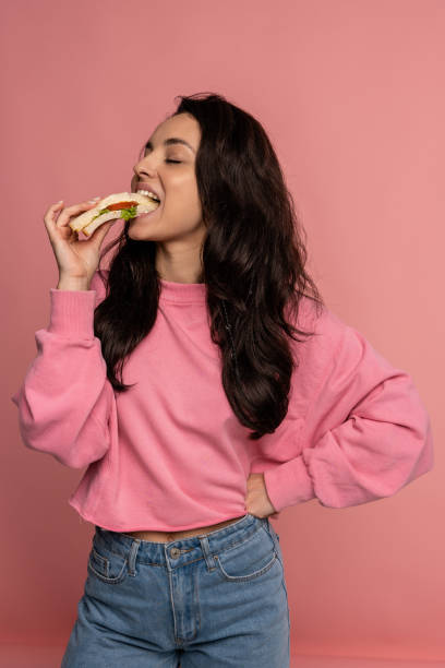 Hungry beautiful young dark-haired Caucasian woman snacking on an appetizing nutritious sandwich in front of the camera. Nourishing nutrition concept