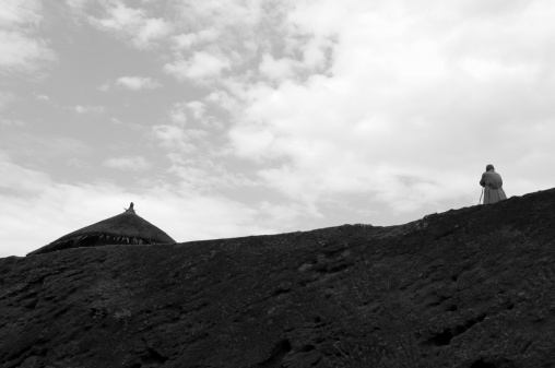 A man leans against his staff on the ridge of a hill in Lalibela, Ethiopia. On the left is the roof of a hut.