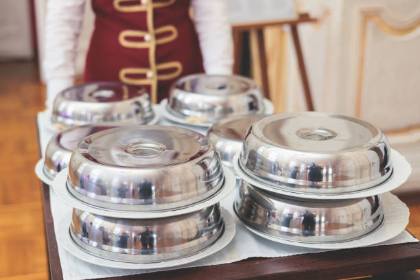 Process of serving luxury dinner in a cloche plate dish with a lid, waiter serving main course meal under silver platter on a banquet in  restaurant or hotel, serving dish food cover