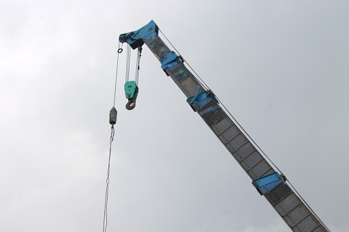 Constructing process of a tower crain. yellow steel truss vertical frame erected by a mobile crane boom. lifting activity. blue sky background. vertical steel wire cables and hoisting system.