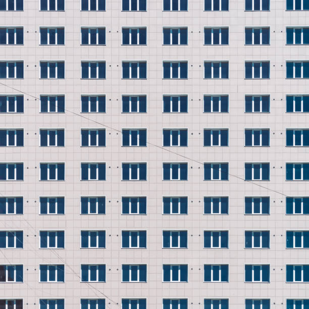 istock Geometric backdrop with lots of window rows. Simple classic design high-rise building. Realistic concept of office building. Apartment house texture background. Many windows on big wall close-up. 1588570524