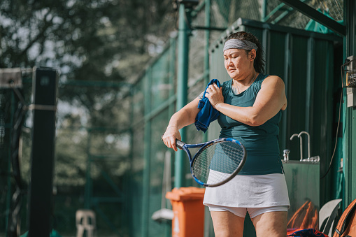 Asian Chinese female tennis player wiping sweat with towel after game at tennis court