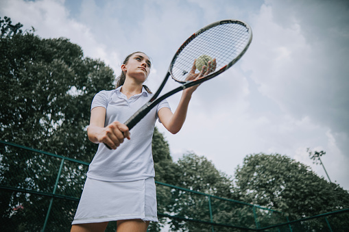 teenage girl tennis player serving in tennis court