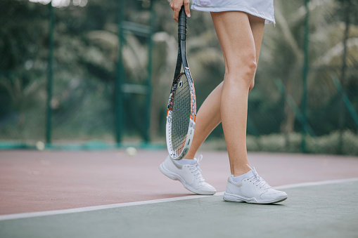 Photo taken in late evening under lights of a yellow tennis ball on blue tennis court with white line and green out of bounds.