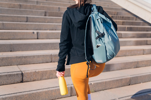rear view of an unrecognizable sportswoman walking up urban stairs with a reusable water bottle in hand, concept of active and sportive lifestyle, copy space for text
