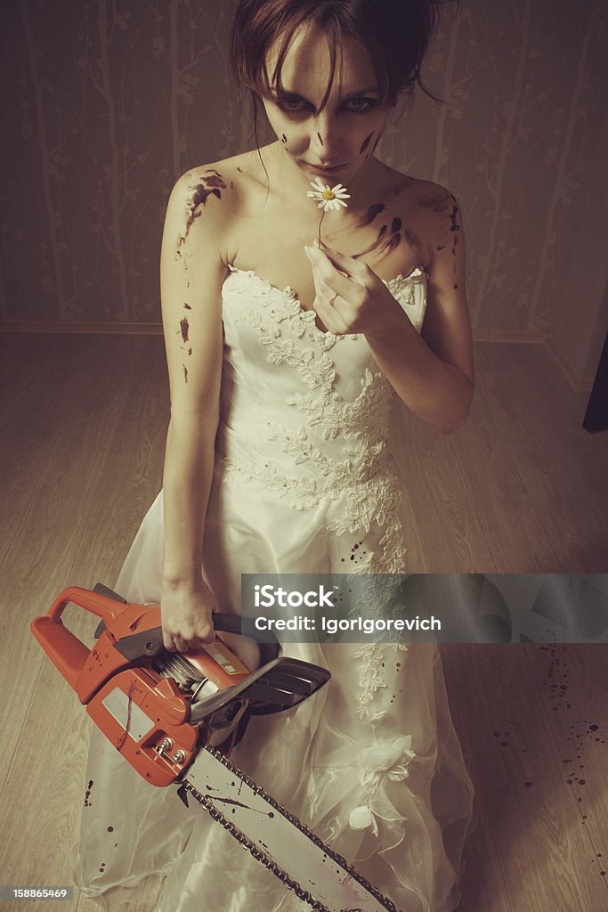 Beauty and blood Pretty young bride standing in the empty room with bloody chainsaw and chamomile Adult Stock Photo