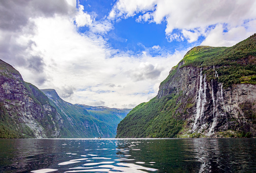 view of the cliff with the Seven Sisters waterfall from the water of Geirangerfjord in Norway. green forest on the rocky slopes of the mountains surrounding the fjord