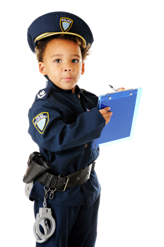 An adorable preschool policeman in uniform, looking up from writing a ticket.  On a white background.