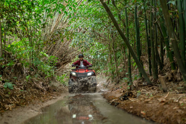 istock Asian guy having fun while driving an atv in the jungle alone. Drive through water in the deep forest. 1588791087