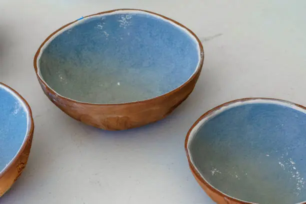 Three handmade brown and red terra cotta clay bowls with blue glaze on the inside. Sitting on a white table.