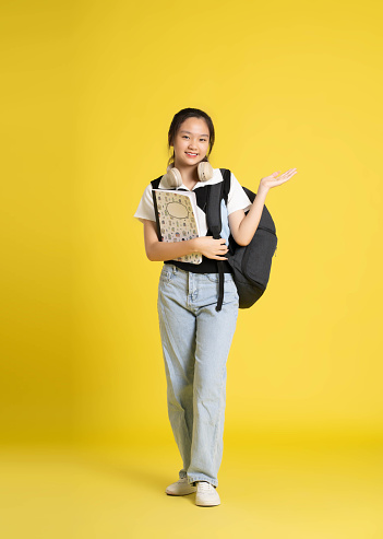 portrait of beautiful asian schoolgirl wearing a backpack on a yellow background