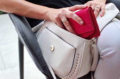 Woman's hand pulling out red wallet from the white bag