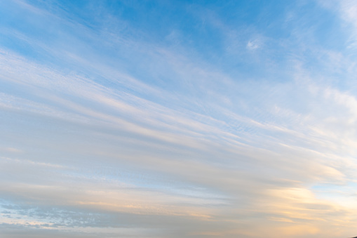 sunset sky with pink clouds, diagonally stripe, grey above. Whispy pink clouds and blue sky diving frame diagonally. Cirrus and cirrocumulus clouds form a colored triangle.