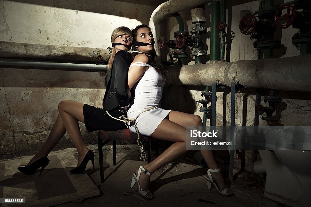 Two Female Hostages Two young female hostages tied up sitting back to back in a dirty basement. Hostage Stock Photo