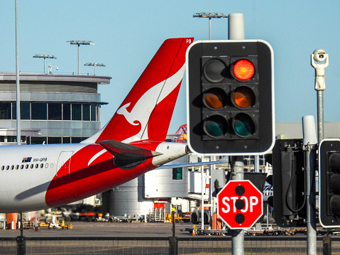 A Qantas Airbus A330-303 plane, registration VH-OPB, is taxiing to the domestic terminal of Sydney Kingsford-Smith Airport having landed as flight QF450 from Melbourne.  In the distance is the domestic terminal.  The \