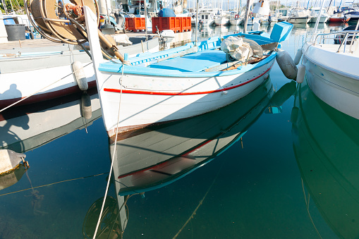 Traditional European fishing boats moored and reflected in calm Antibes harbour in Mediterranaean France.
