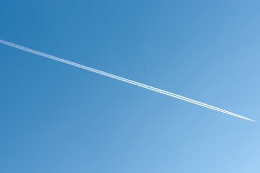Double thin vapor trails diagonally across blue clear sky