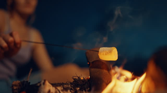 SLO MO Close-up of Blurred Woman Roasting Marshmallow on Skewer over Bonfire at Night