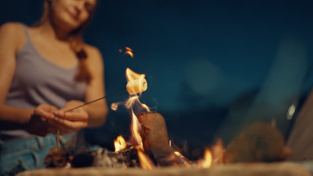 SLO MO Woman Roasts a Marshmallow on Skewer over Crackling Bonfire in Serene Countryside at Night