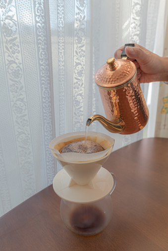 A scene of crushing coffee beans, setting them in a dripper, and pouring hot water. The coffee grounds expand due to the hot water, allowing the delicious components to be extracted slowly and thoroughly.